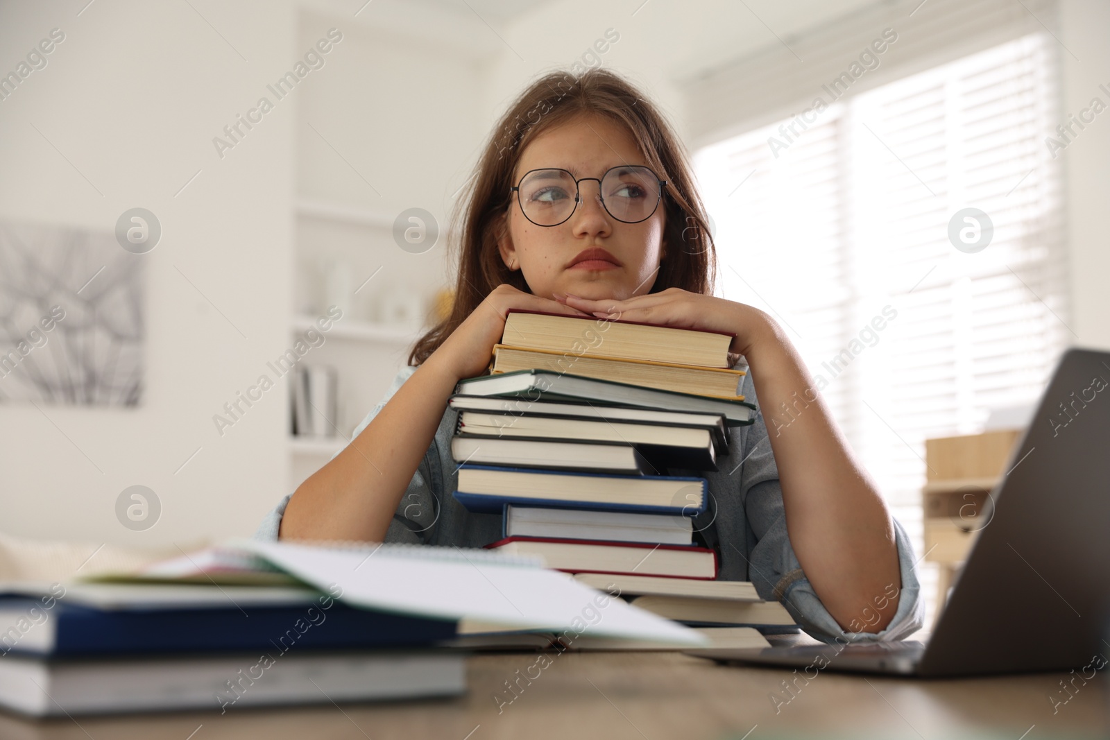 Tired student with stack of books preparing for exam at table indoors Photo of Tired student with stack of books preparing for exam at table indoors