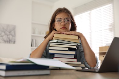 Photo of Tired student with stack of books preparing for exam at table indoors
