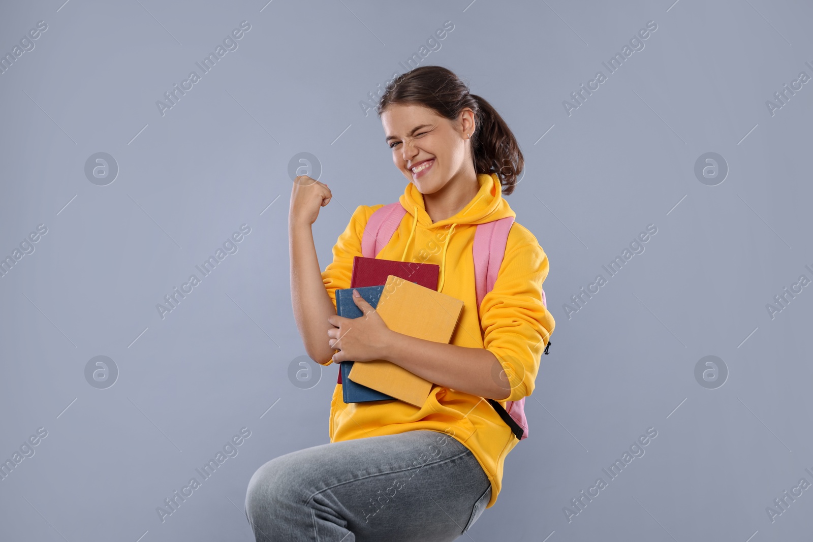 Student with notebooks feeling happy about her good exam result on gray background Photo of Student with notebooks feeling happy about her good exam result on gray background