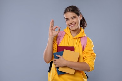 Photo of Student with notebooks showing OK gesture before exam on gray background