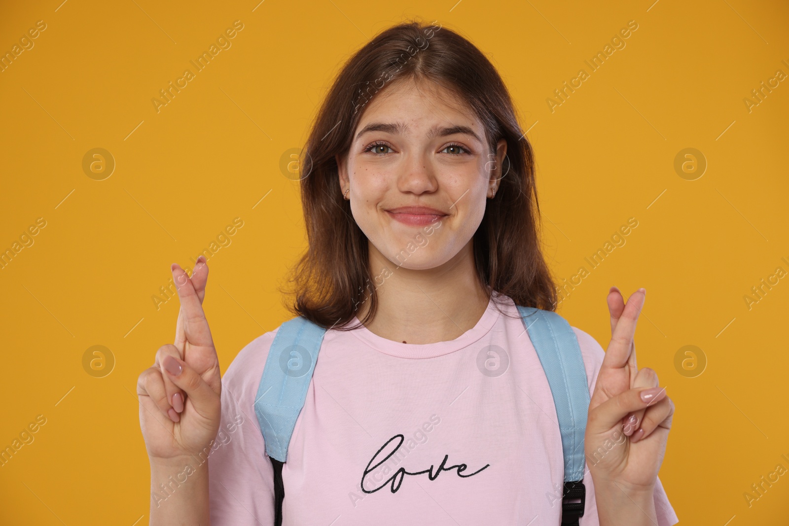 Excited student crossing fingers on orange background. Hope for good exam result Photo of Excited student crossing fingers on orange background. Hope for good exam result