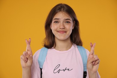 Photo of Excited student crossing fingers on orange background. Hope for good exam result