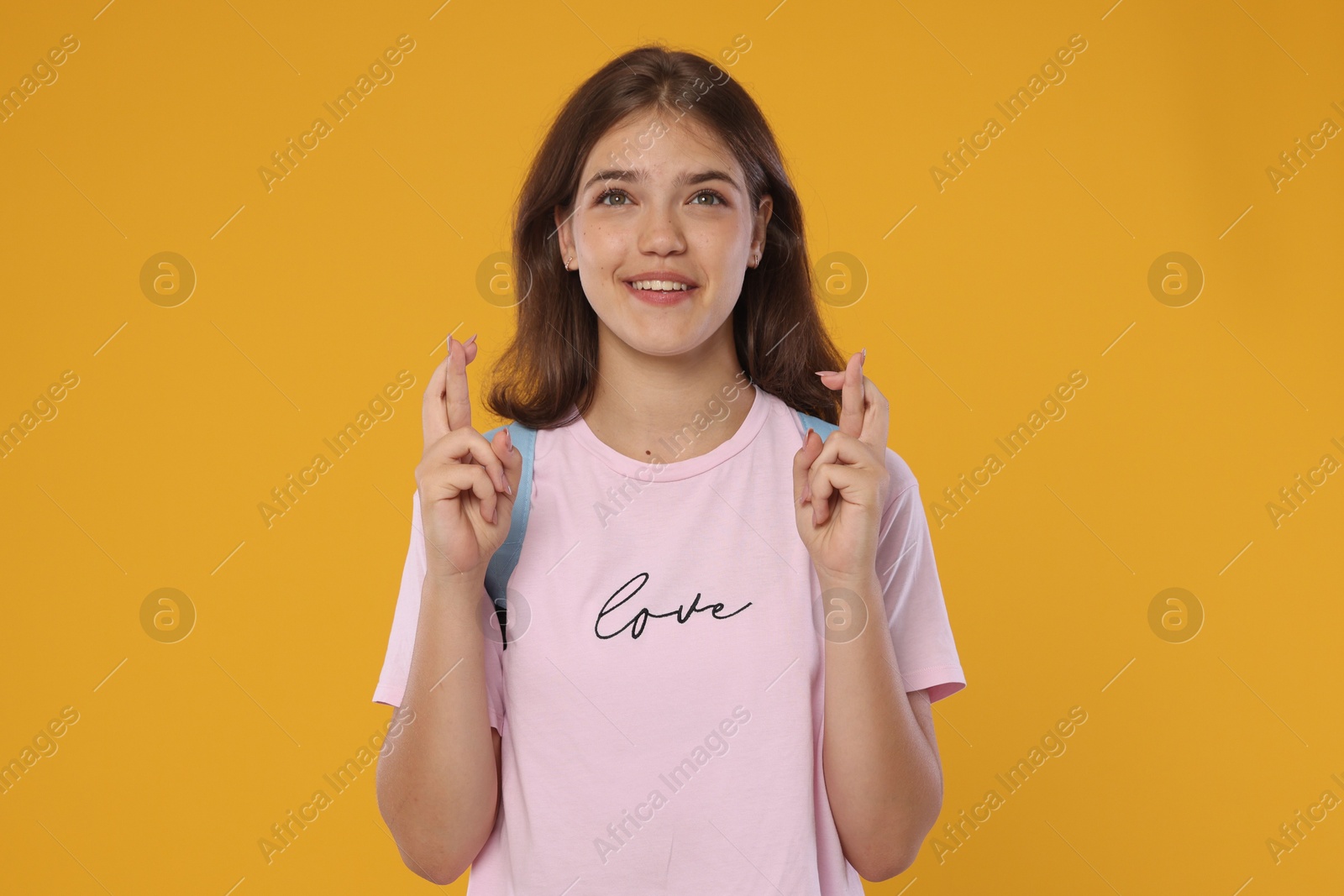 Excited student crossing fingers on orange background. Hope for good exam result Photo of Excited student crossing fingers on orange background. Hope for good exam result