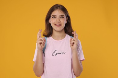 Photo of Excited student crossing fingers on orange background. Hope for good exam result
