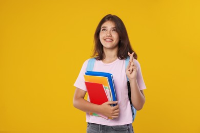 Photo of Student with notebooks crossing fingers on orange background. Hope for good exam result
