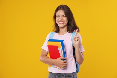 Photo of Student with notebooks crossing fingers on orange background. Hope for good exam result