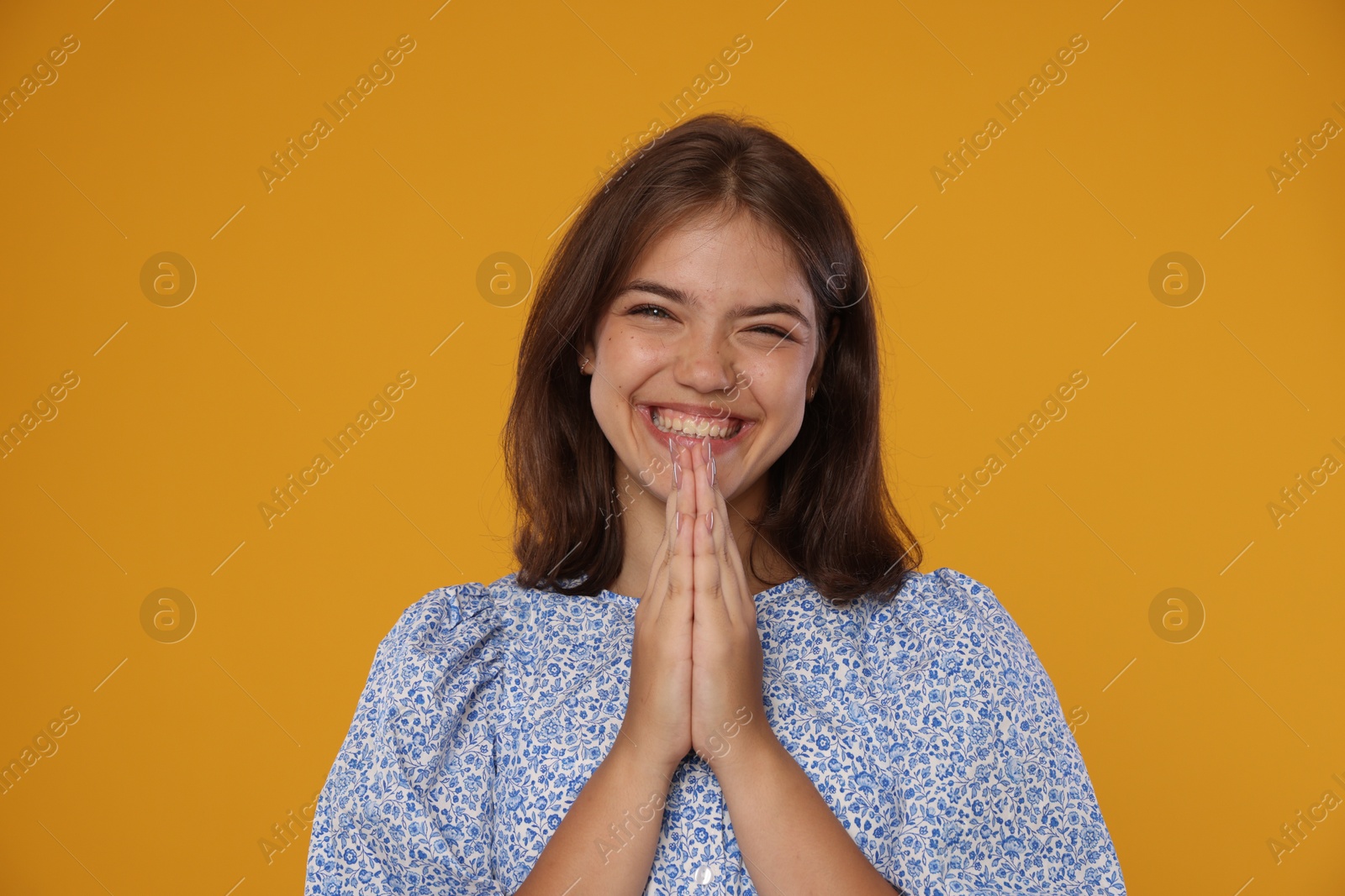 Excited student with clasped hands happy about her good exam result on orange background Photo of Excited student with clasped hands happy about her good exam result on orange background