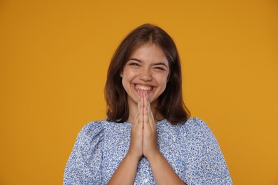Photo of Excited student with clasped hands happy about her good exam result on orange background