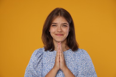 Photo of Student with clasped hands on orange background. Hope for good exam result
