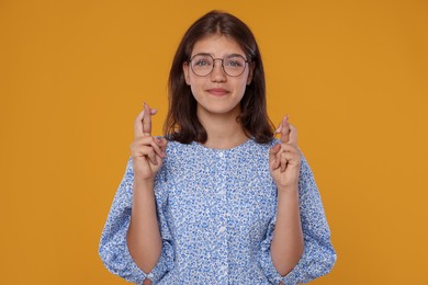Photo of Student crossing fingers on orange background. Hope for good exam result
