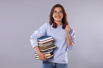 Photo of Student with stack of books feeling happy about her good exam result on gray background