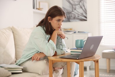 Photo of Student feeling unhappy about her exam result at wooden table with laptop indoors