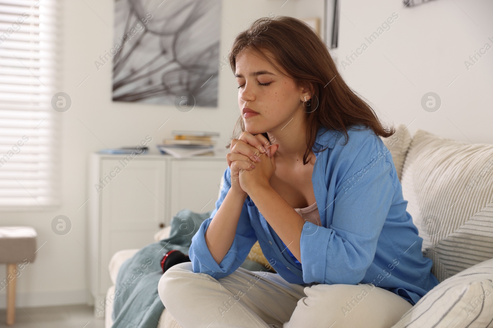 Student praying for good exam result on sofa indoors Photo of Student praying for good exam result on sofa indoors