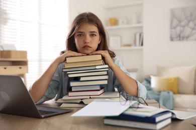 Photo of Tired student with stack of books preparing for exam at table indoors