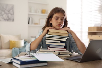 Photo of Tired student with stack of books preparing for exam at table indoors