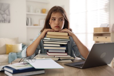 Photo of Tired student with stack of books preparing for exam at table indoors