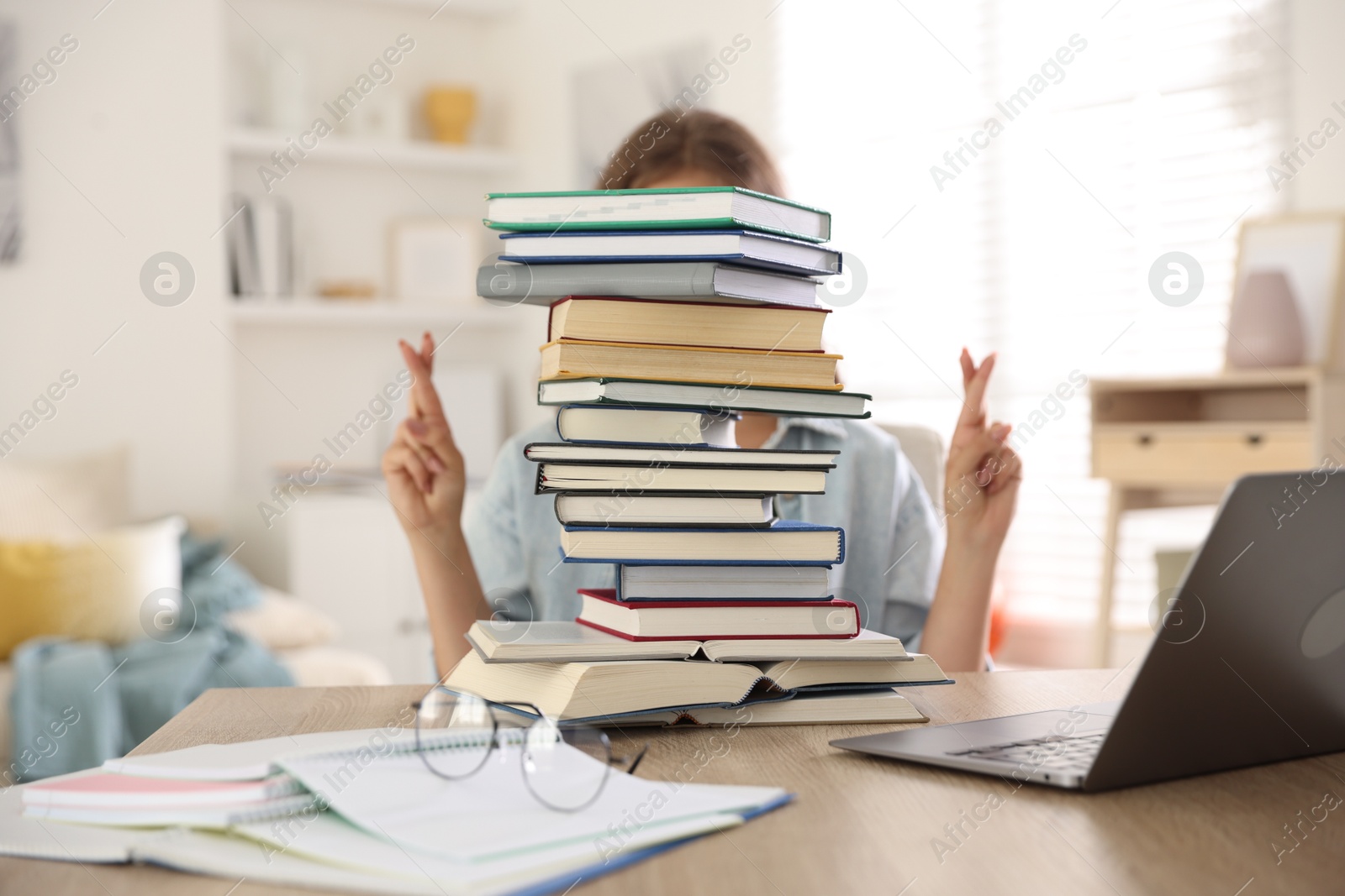 Student crossing fingers behind stack of books at table indoors. Hope for good exam result Photo of Student crossing fingers behind stack of books at table indoors. Hope for good exam result