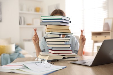 Photo of Student crossing fingers behind stack of books at table indoors. Hope for good exam result