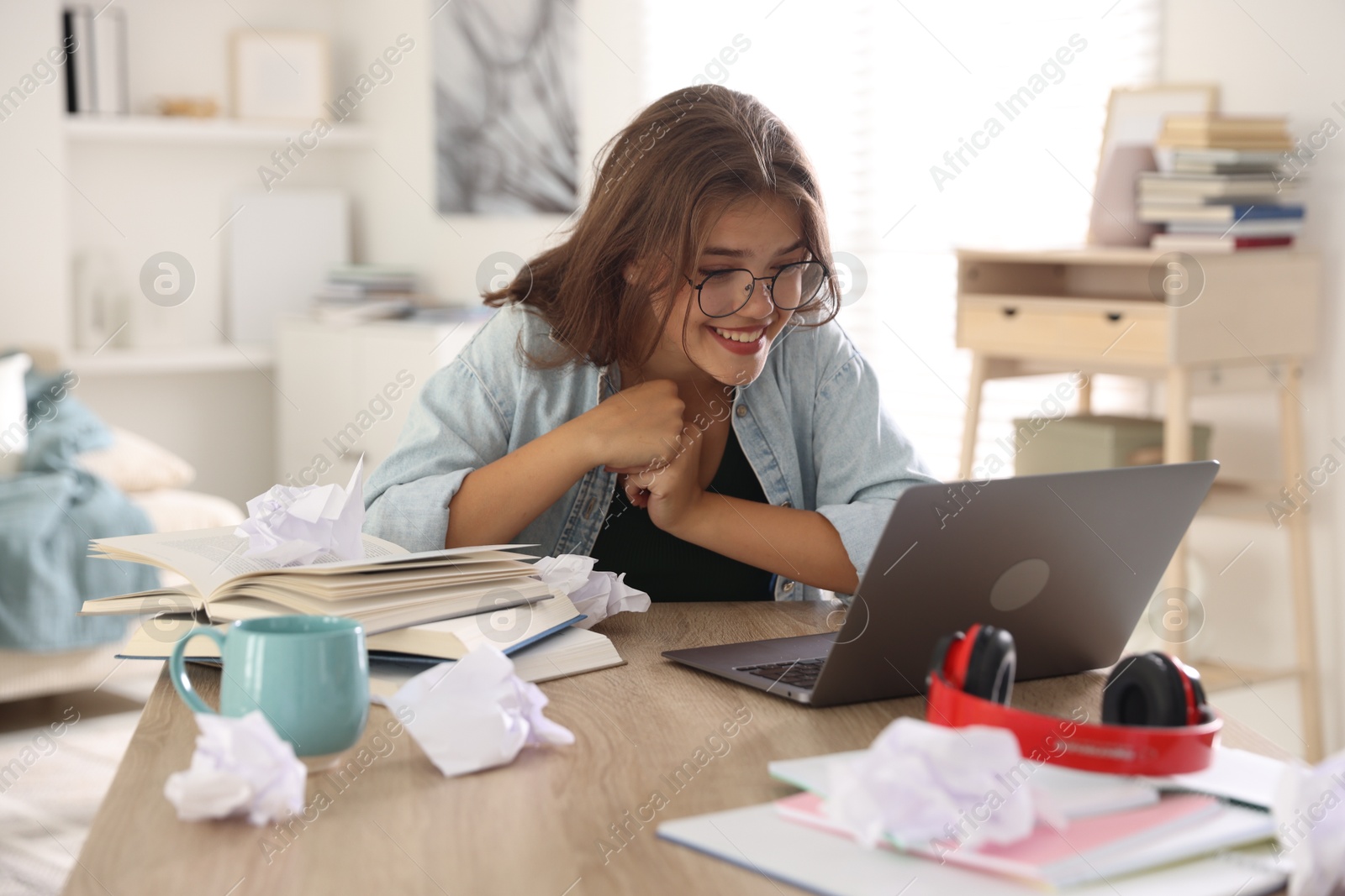 Student feeling happy about her good exam result at table with laptop indoors Photo of Student feeling happy about her good exam result at table with laptop indoors