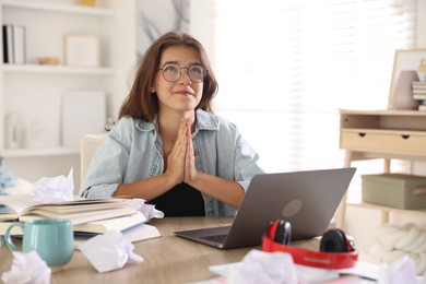Photo of Student praying for good exam result at table indoors