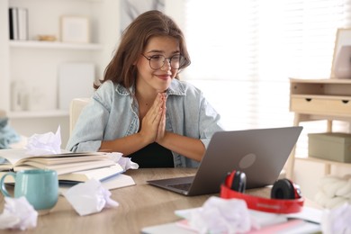 Photo of Student praying for good exam result at table indoors