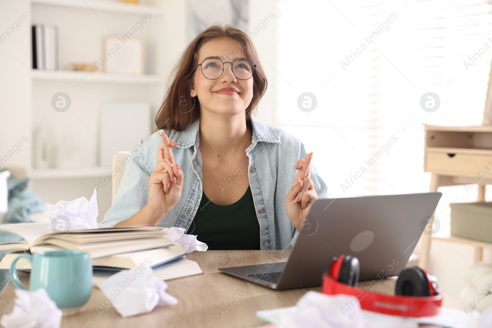 Student crossing fingers at table with laptop indoors. Hope for good exam result Photo of Student crossing fingers at table with laptop indoors. Hope for good exam result