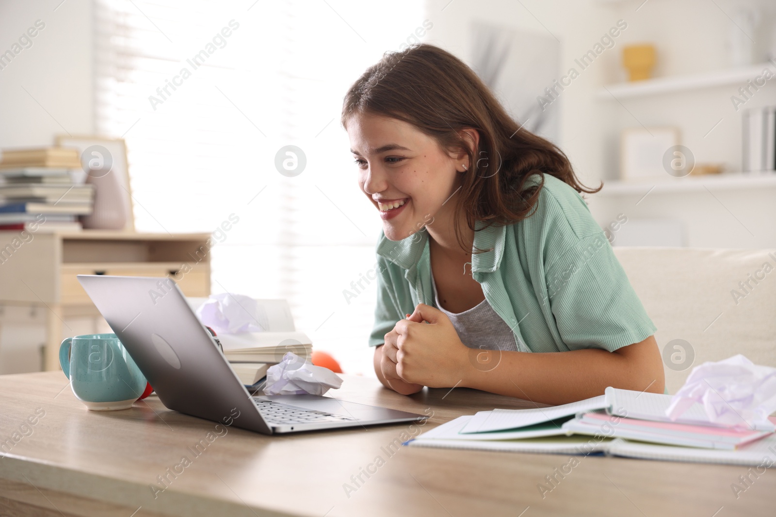 Student feeling happy about her good exam result at table with laptop indoors Photo of Student feeling happy about her good exam result at table with laptop indoors