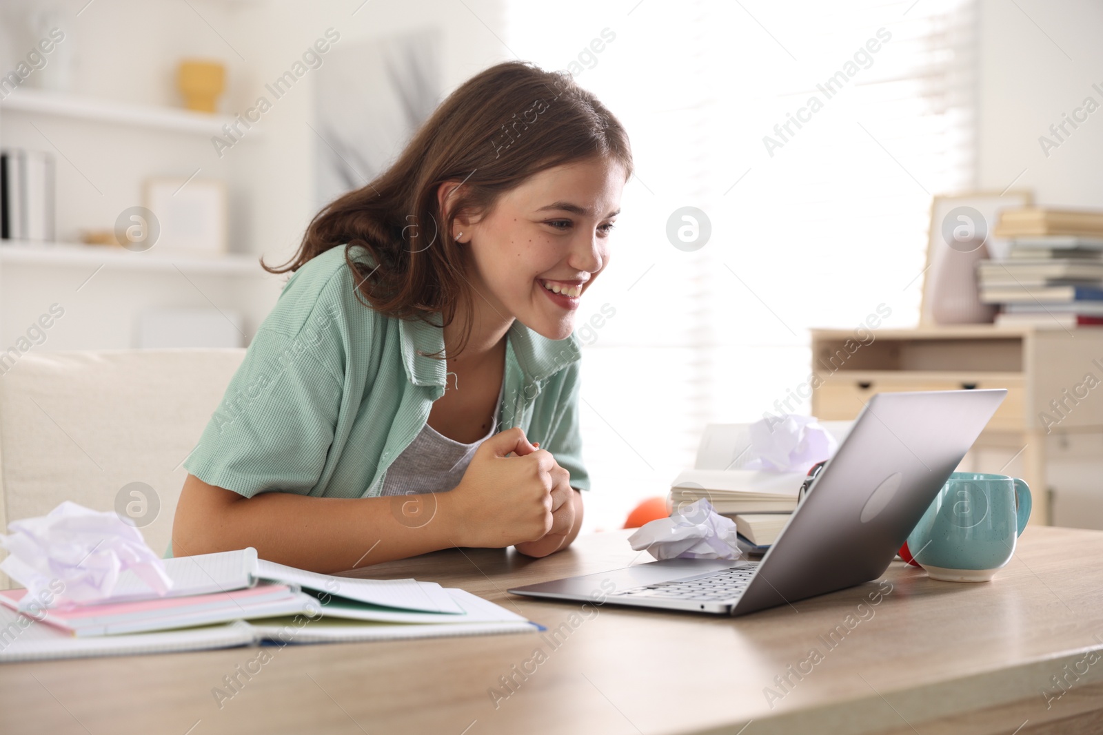 Student feeling happy about her good exam result at table with laptop indoors Photo of Student feeling happy about her good exam result at table with laptop indoors