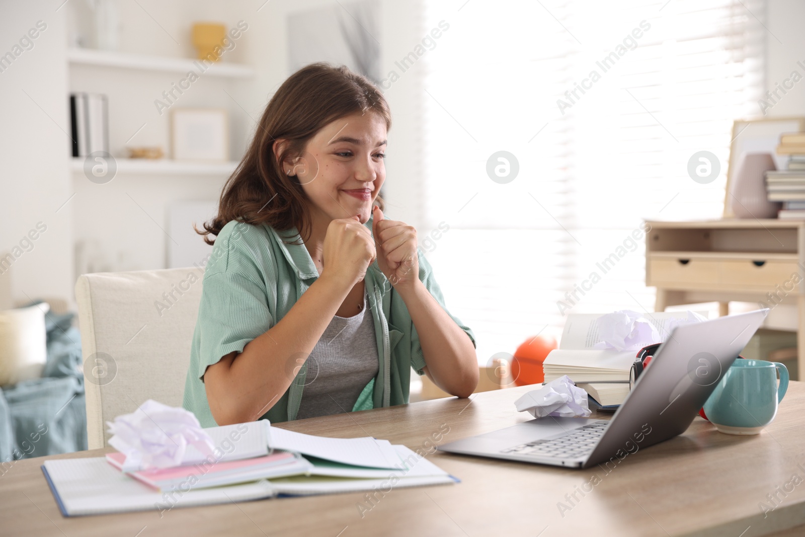 Student feeling happy about her good exam result at table with laptop indoors Photo of Student feeling happy about her good exam result at table with laptop indoors