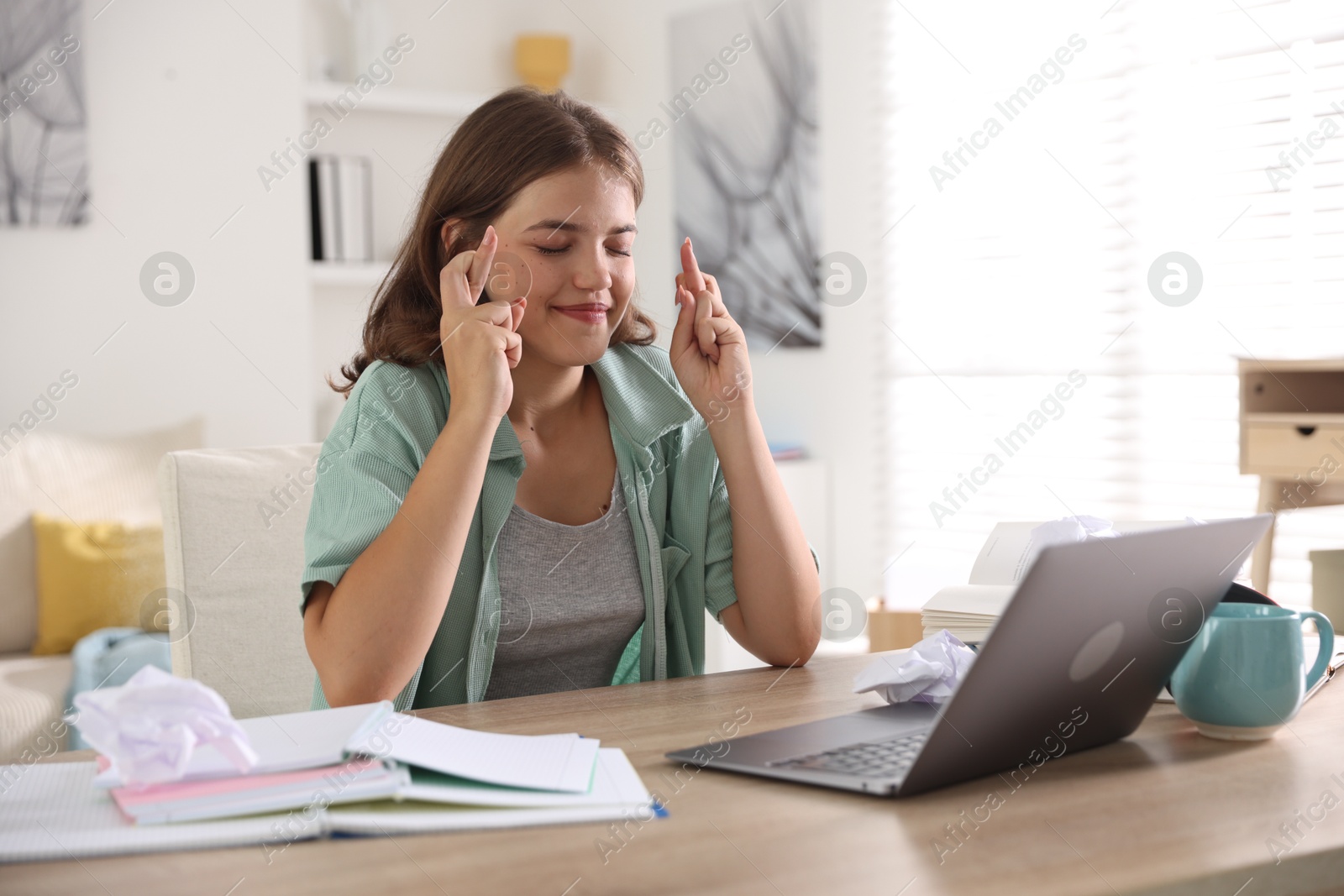 Student crossing fingers at table with laptop indoors. Hope for good exam result Photo of Student crossing fingers at table with laptop indoors. Hope for good exam result