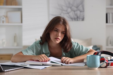 Photo of Tired student preparing for exam at table indoors