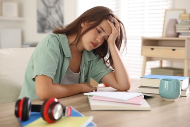 Photo of Tired student preparing for exam at table indoors
