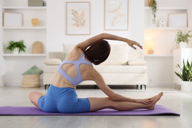 Photo of Woman in sportswear stretching on mat at home, back view
