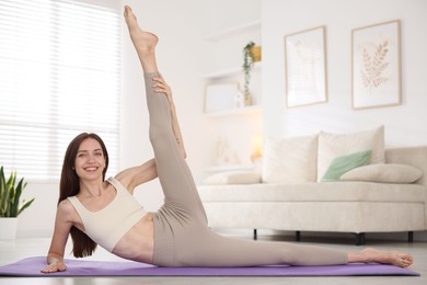 Photo of Smiling woman in sportswear stretching on mat at home