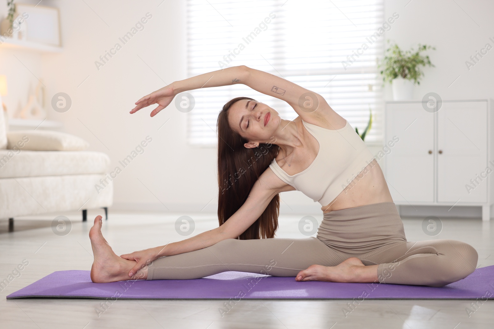 Young woman in sportswear stretching on mat at home Photo of Young woman in sportswear stretching on mat at home