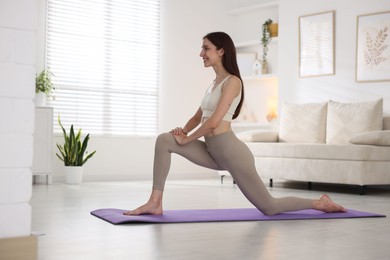Photo of Smiling woman in sportswear stretching on mat at home