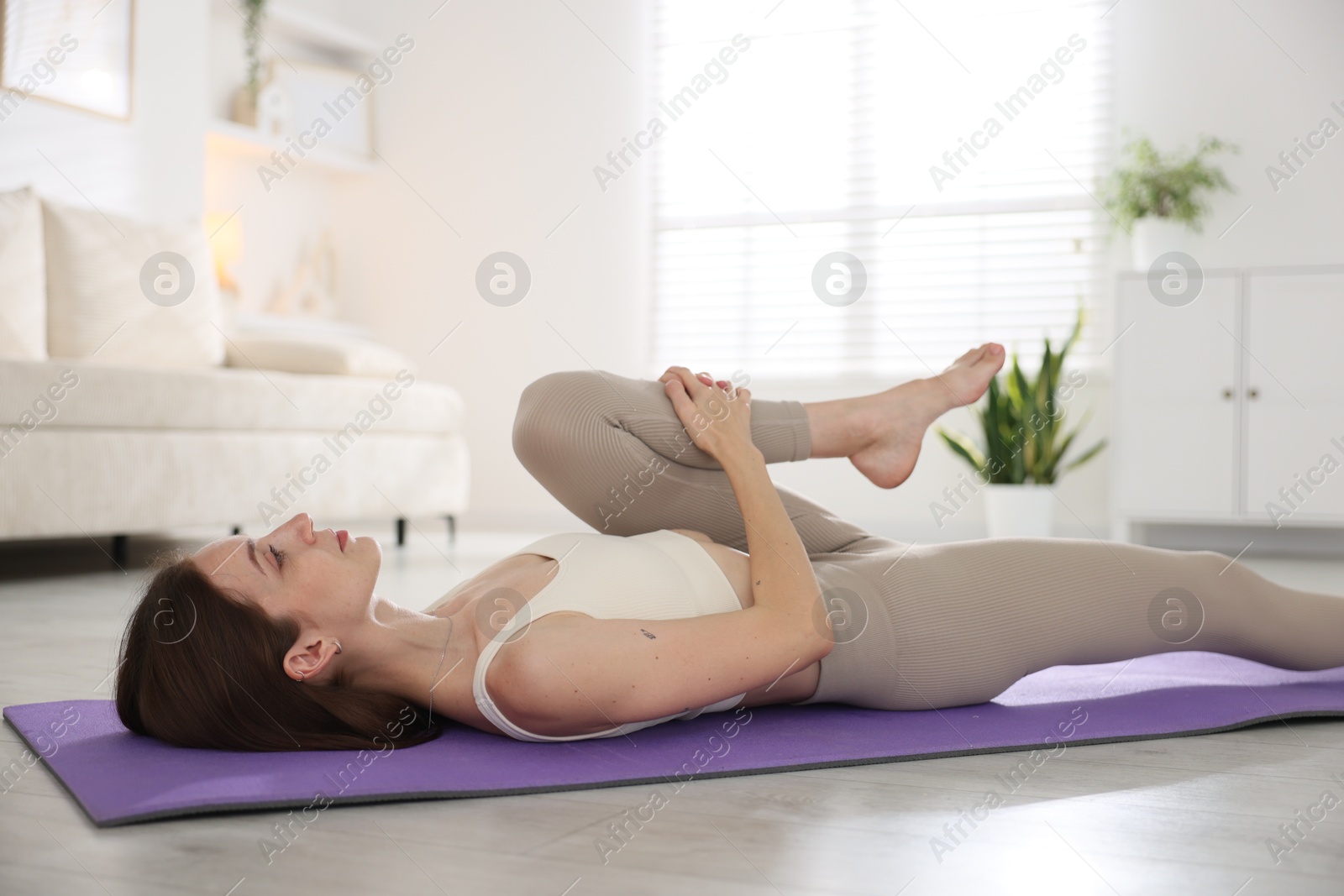 Young woman in sportswear stretching on mat at home Photo of Young woman in sportswear stretching on mat at home