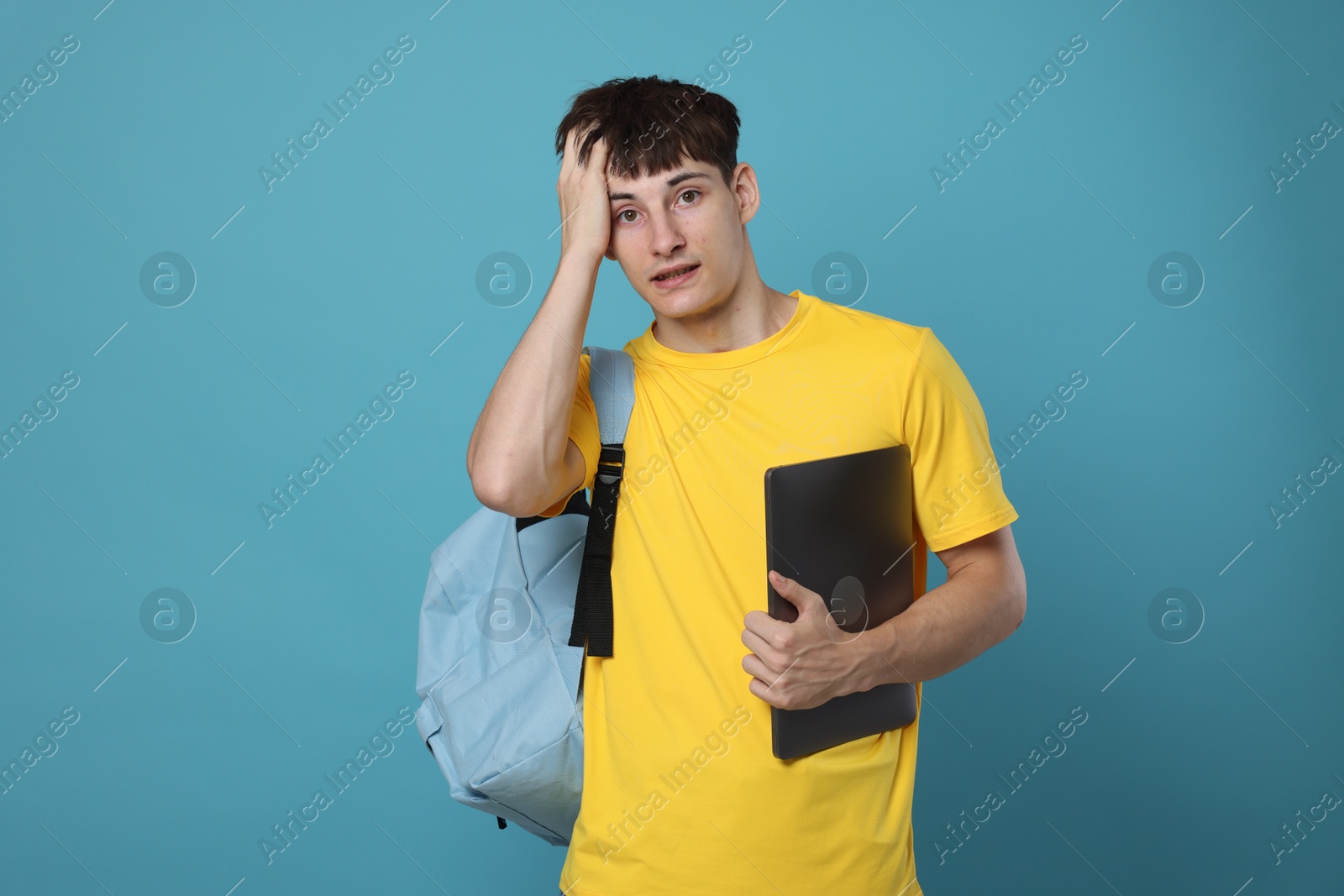 Worried student with laptop on light blue background Photo of Worried student with laptop on light blue background