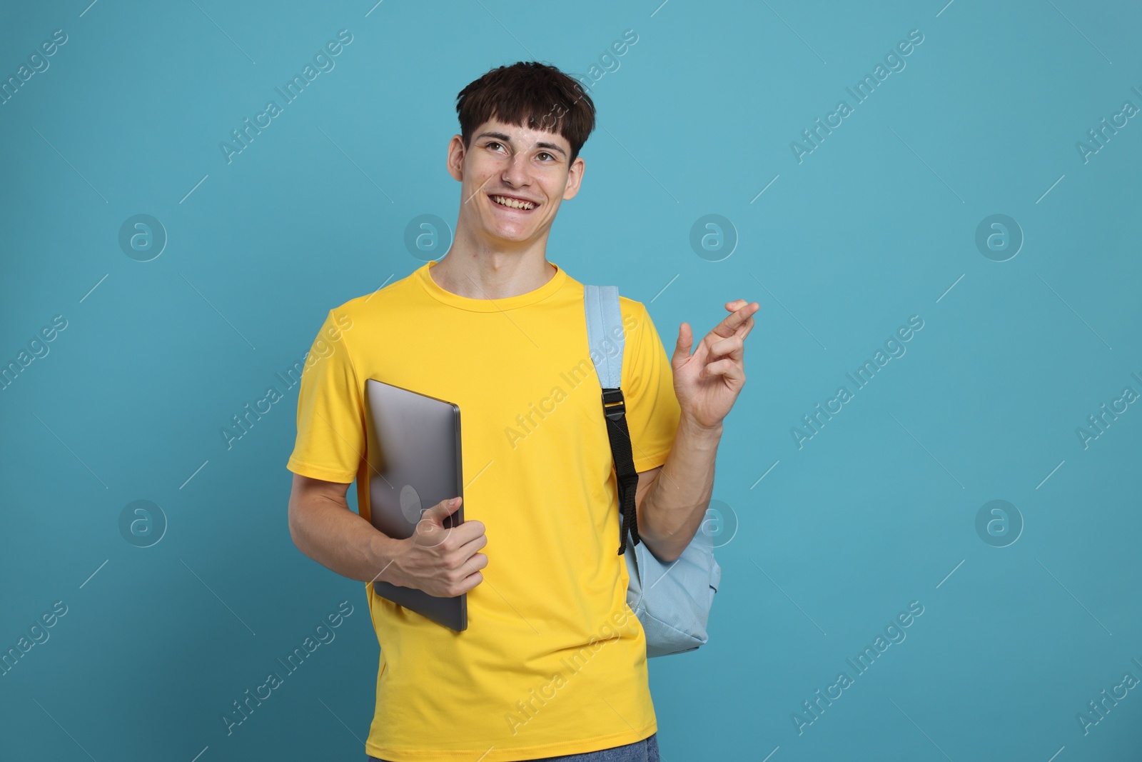 Happy student crossing fingers for good exam result on light blue background Photo of Happy student crossing fingers for good exam result on light blue background