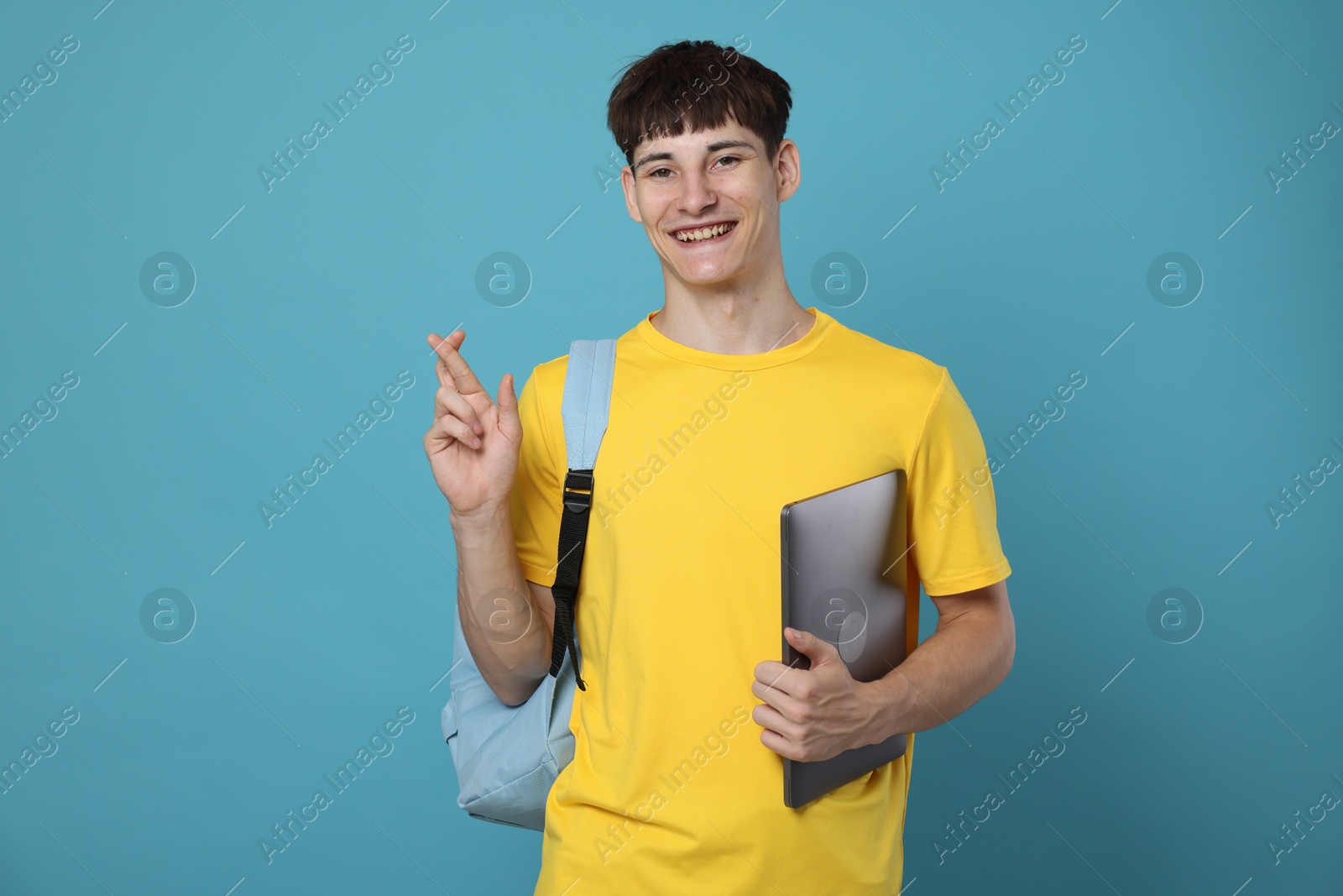 Happy student crossing fingers for good exam result on light blue background Photo of Happy student crossing fingers for good exam result on light blue background