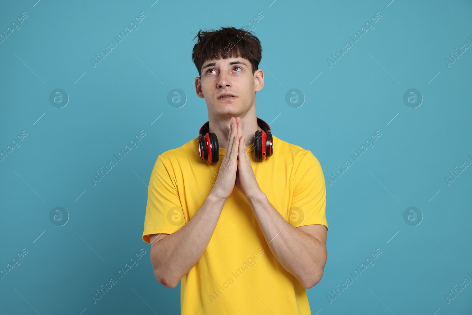 Worried student with clasped hands praying for good exam result on light blue background Photo of Worried student with clasped hands praying for good exam result on light blue background