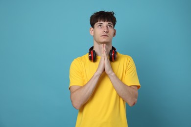 Photo of Worried student with clasped hands praying for good exam result on light blue background