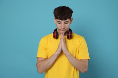 Photo of Worried student with clasped hands praying for good exam result on light blue background