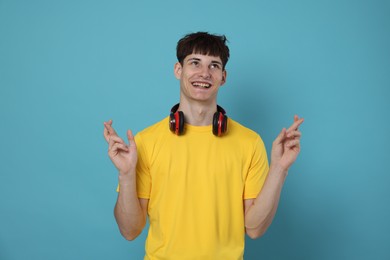 Photo of Happy student crossing fingers for good exam result on light blue background