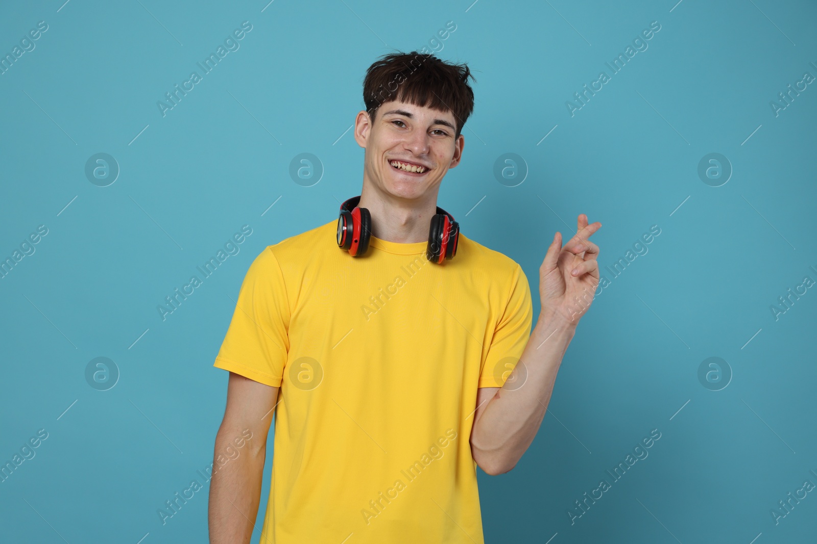 Happy student crossing fingers for good exam result on light blue background Photo of Happy student crossing fingers for good exam result on light blue background