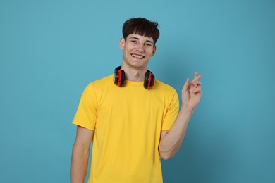 Photo of Happy student crossing fingers for good exam result on light blue background
