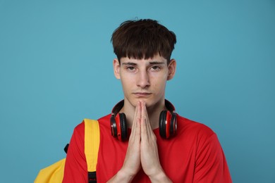 Photo of Worried student with clasped hands praying for good exam result on light blue background
