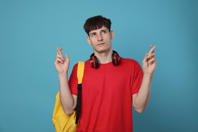 Photo of Worried student crossing fingers for good exam result on light blue background