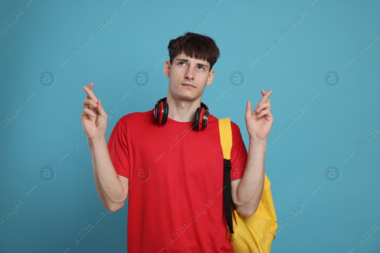 Worried student crossing fingers for good exam result on light blue background Photo of Worried student crossing fingers for good exam result on light blue background