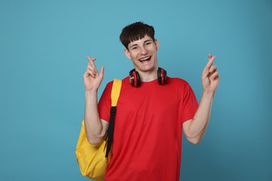Photo of Happy student crossing fingers for good exam result on light blue background